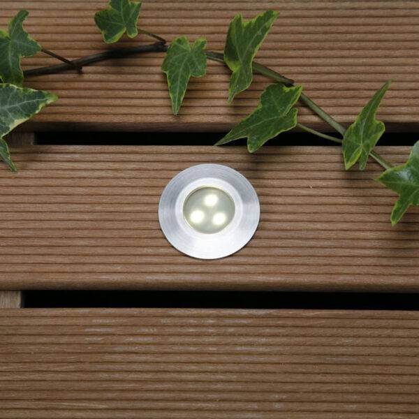 Installed ALPHA warm white decklight on a wooden deck, surrounded by greenery for a natural outdoor ambiance