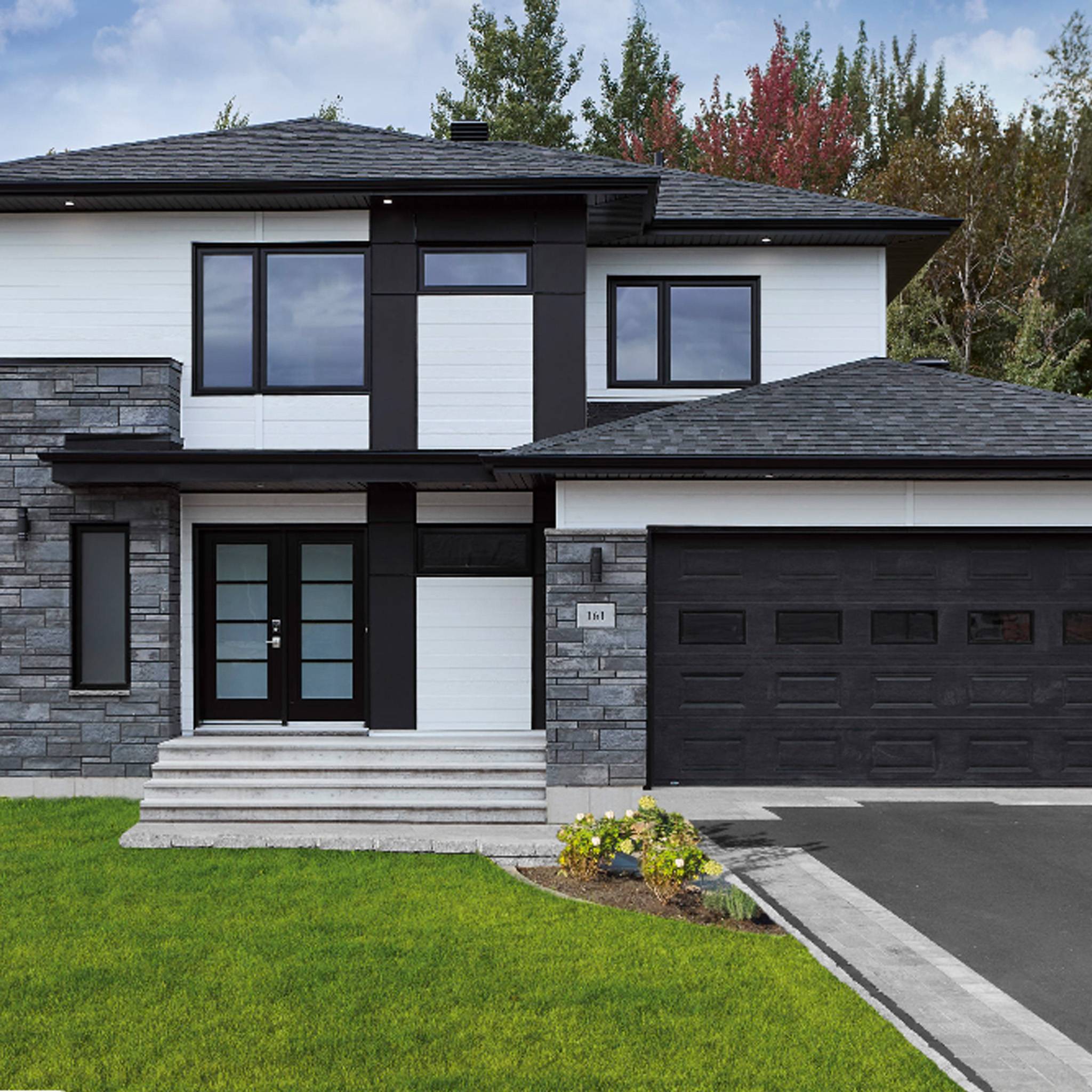 Modern two-story home featuring Maibec genuine wood siding in a striking combination of white and black, complemented by stone accents and a black garage door.