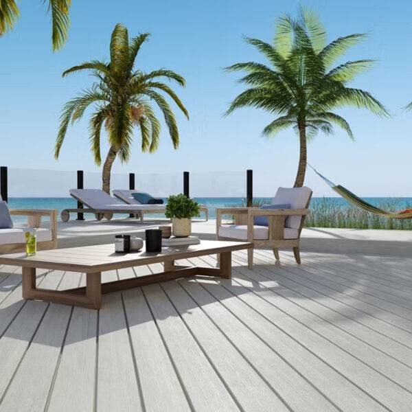 A stylish outdoor deck crafted with Trex Lineage Salt Flat decking, offering a cool, neutral color palette that blends seamlessly with a tropical coastal setting. Features lounge chairs, palm trees, and ocean views, highlighting the decking’s weather-resistant and low-maintenance benefits.
