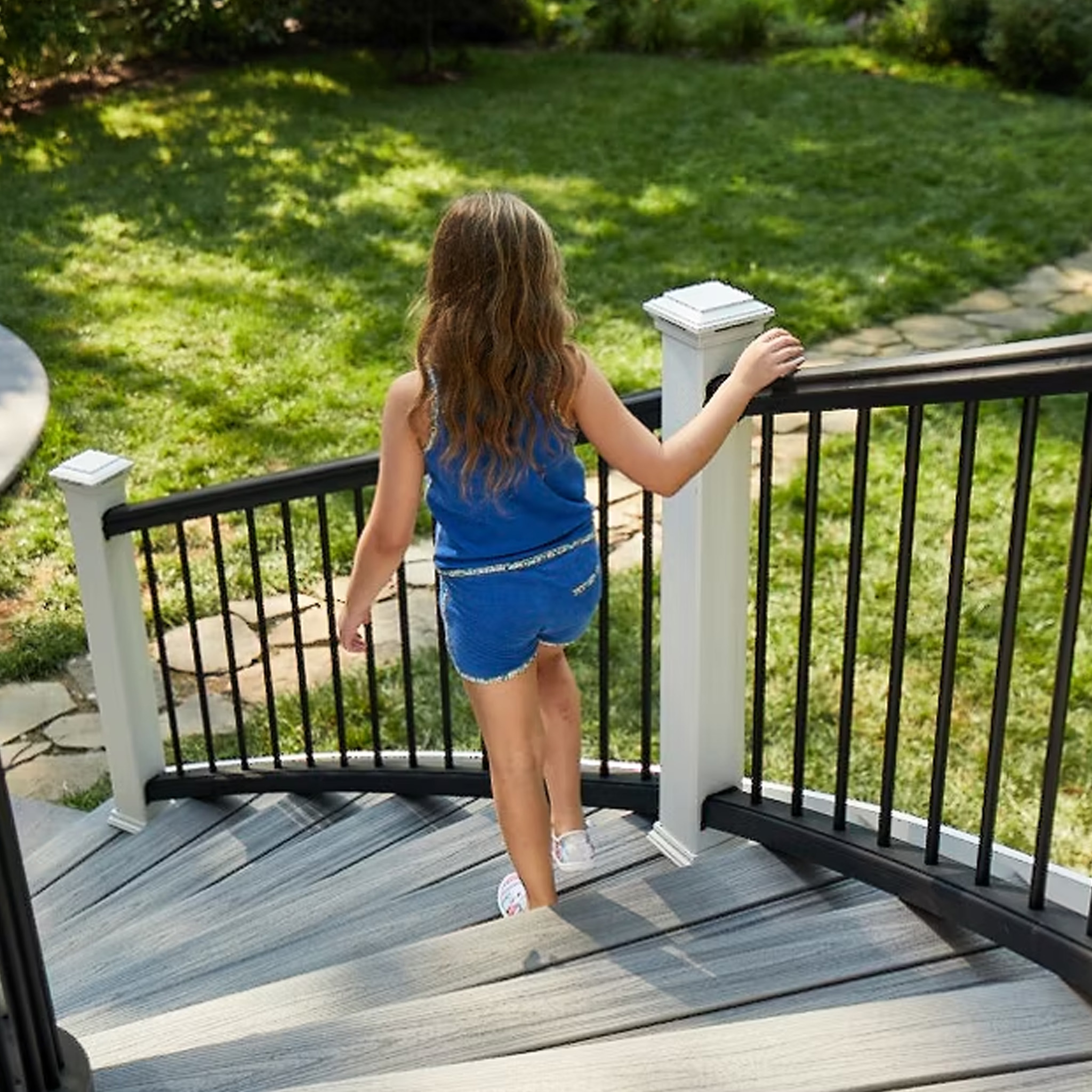 Girl walking down a curved staircase with TREX Transcend railing in black with white posts and balusters.